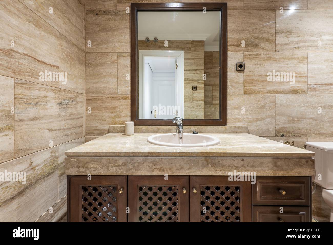 Salle de bains avec murs carrelés de marbre, miroir encadré en bois et meuble-lavabo en marbre avec évier en porcelaine blanche Banque D'Images