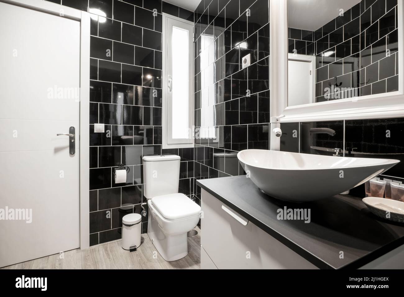 Salle de bains avec murs carrelés de noir, miroir encadré blanc sur le