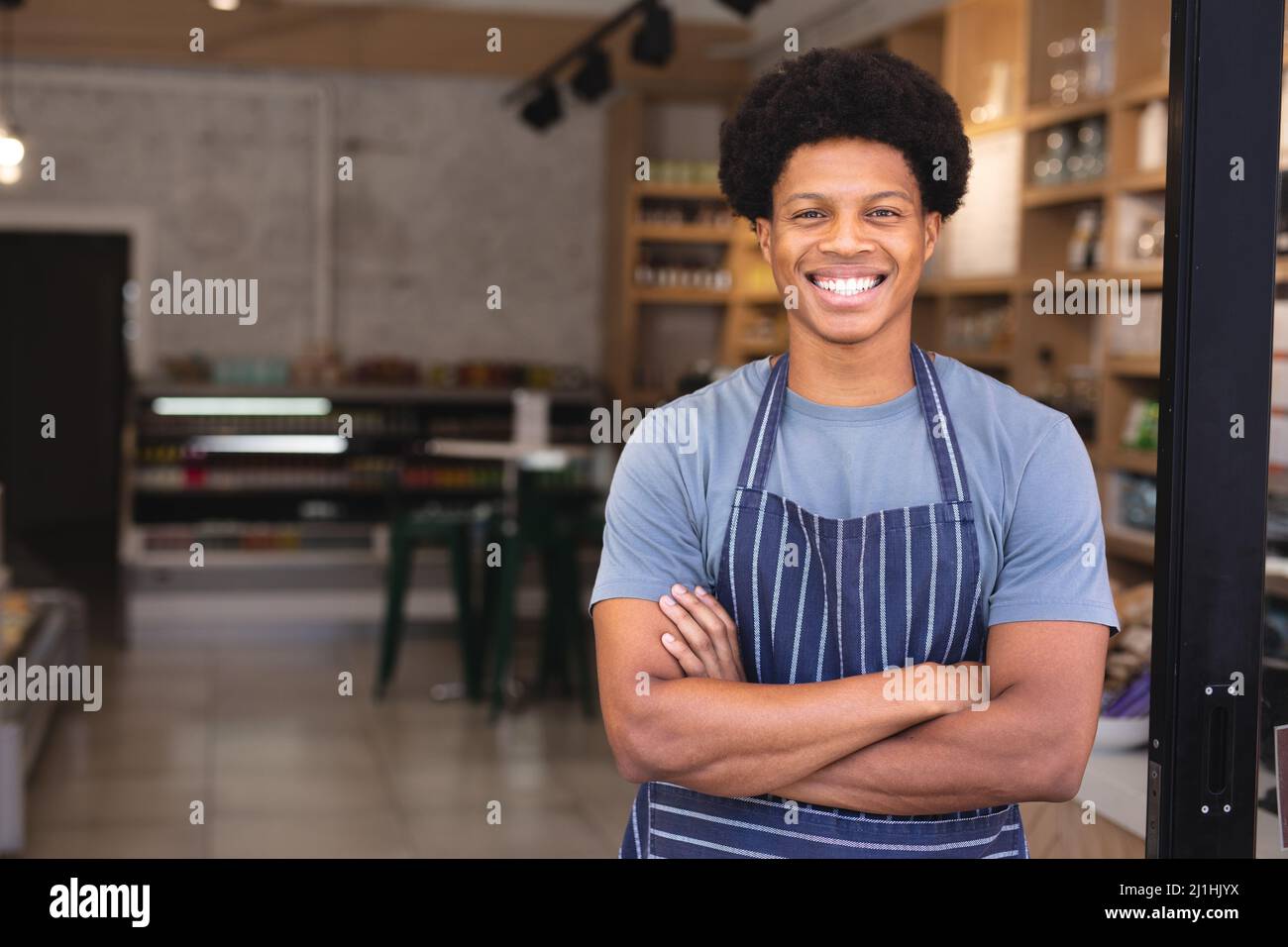 Portrait d'un jeune homme afro-américain heureux avec les bras croisés portant un tablier au café-restaurant. Non modifié, culture de café, les gens et l'occupation con Banque D'Images