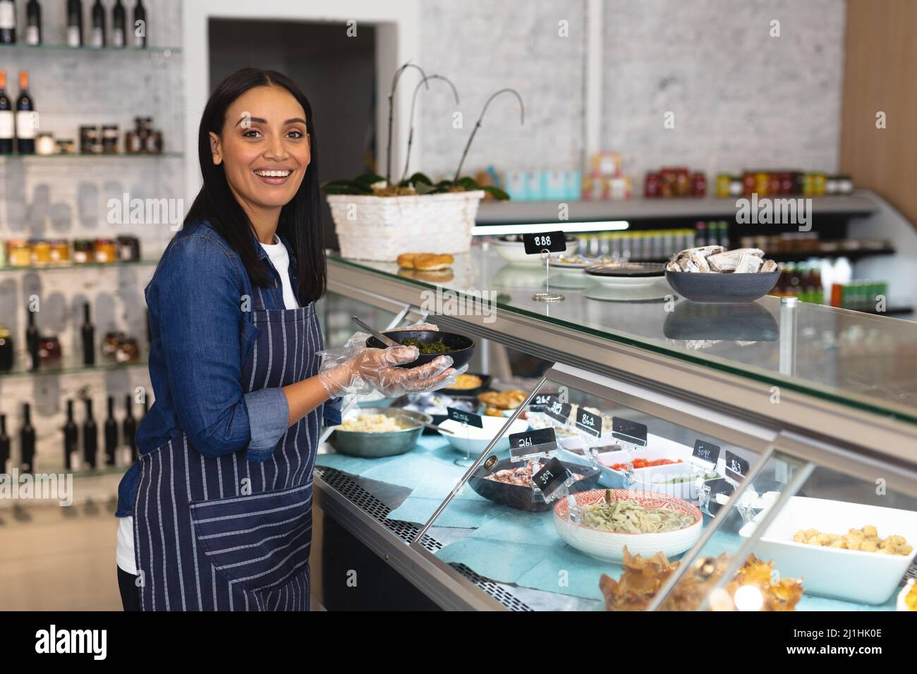 Portrait d'une jeune femme caucasienne souriante tenant un bol par un cabinet exposé dans un café. Non modifié, culture de café, personnes et occupation con Banque D'Images