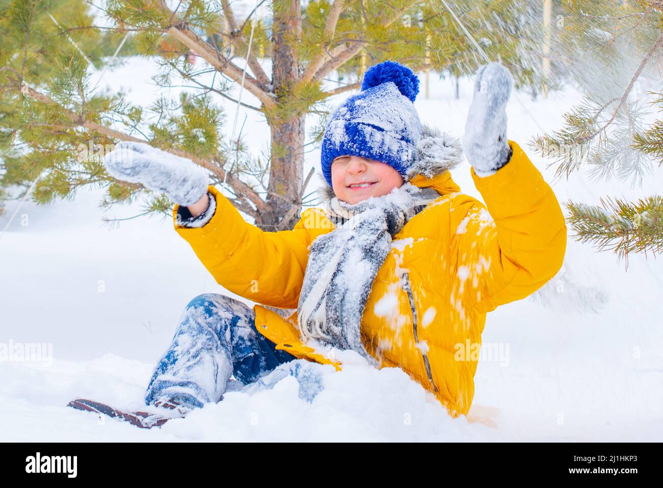 un garçon dans une veste jaune et un chapeau bleu est couché dans la neige Banque D'Images