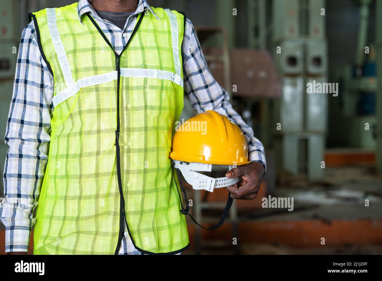 Gros plan d'un travailleur de l'industrie debout en tenant un casque de sécurité en usine - concept de matériel de travail, mesures de sécurité et travail à col bleu. Banque D'Images
