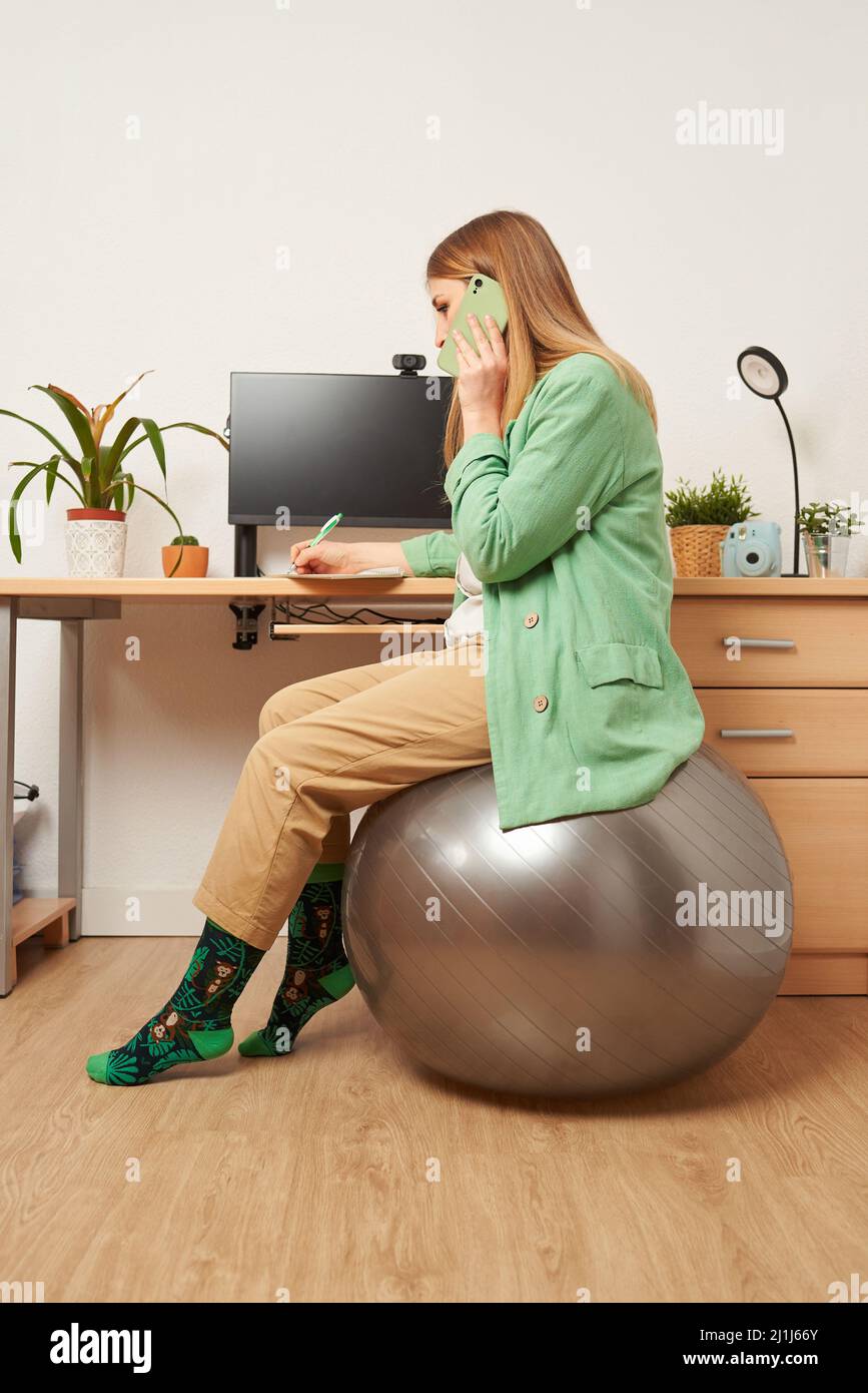 Une femme travaillant à la maison utilise le ballon de fitness comme chaise Banque D'Images