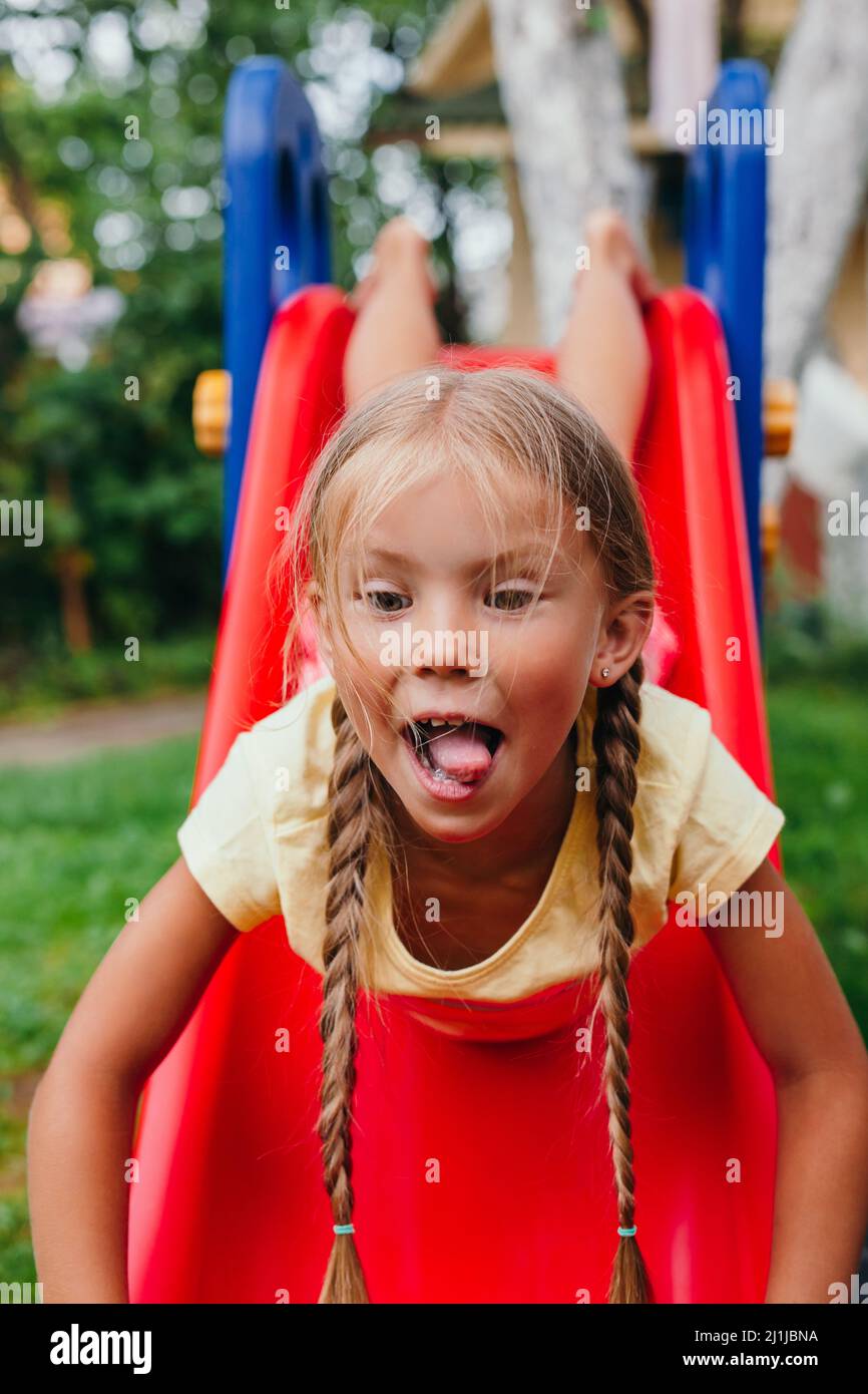 Petite fille drôle jouant sur un toboggan à une aire de jeux. Enfance. L'été Banque D'Images