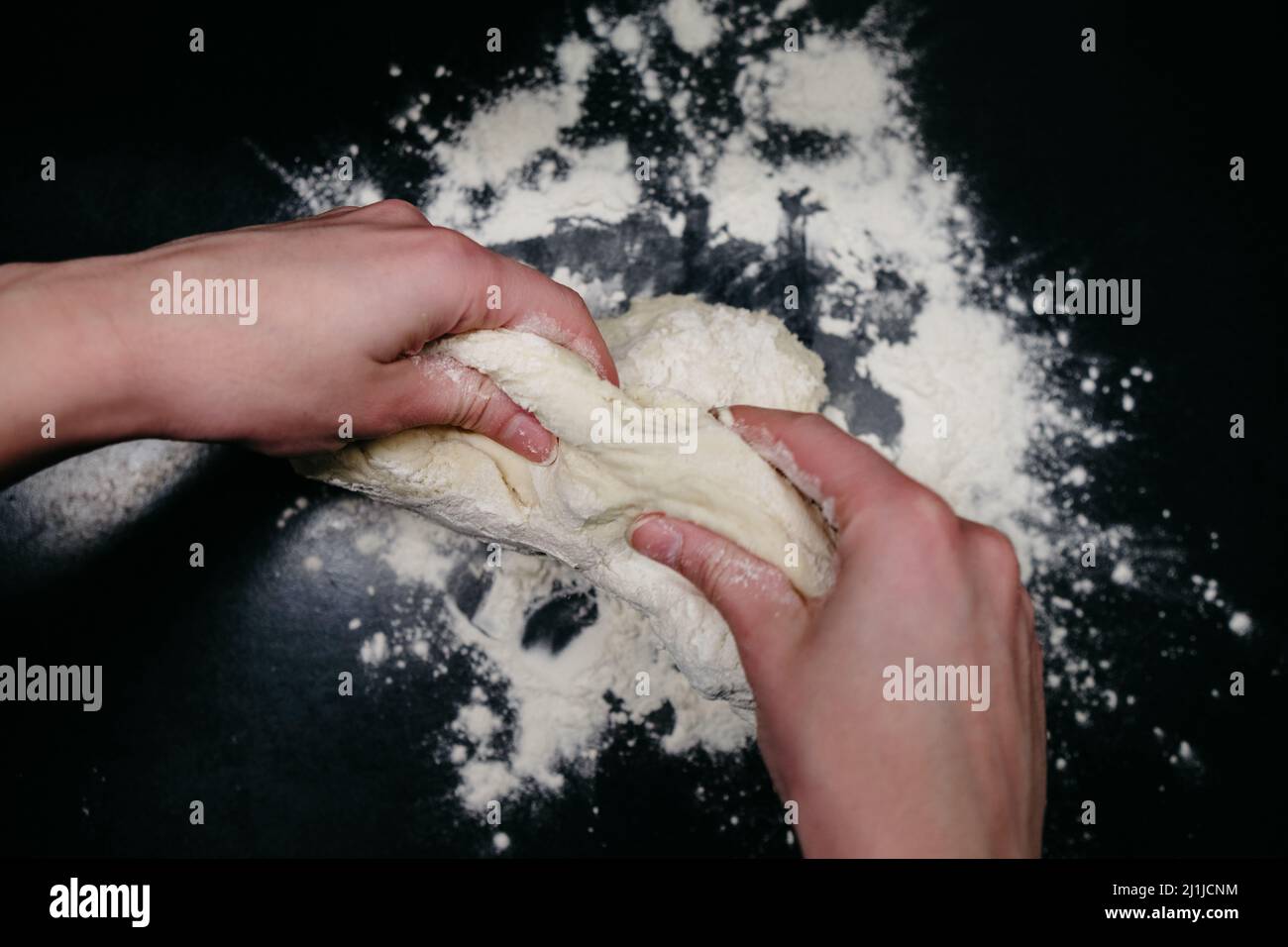 Pâte à pizza sur une table noire avec les mains Banque D'Images