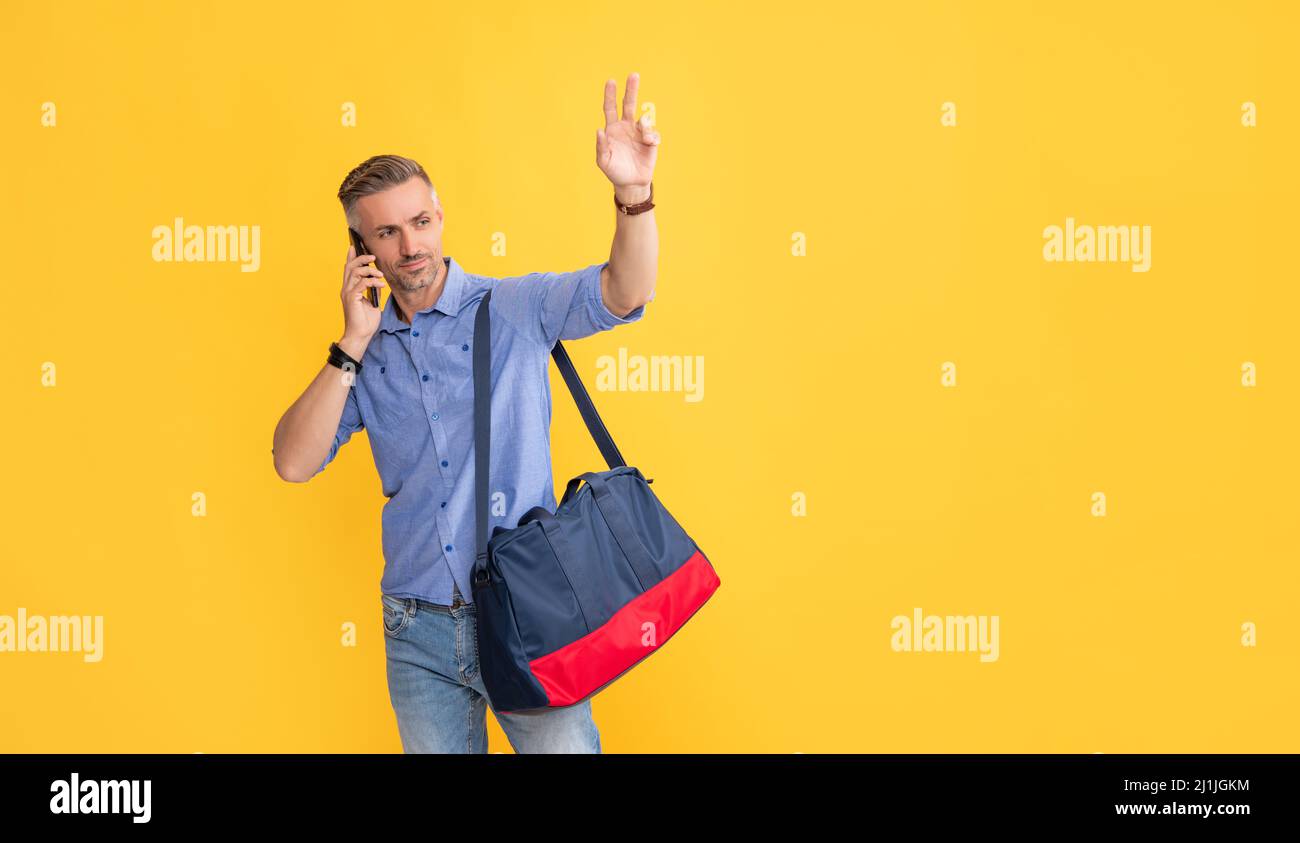 homme parlant sur un smartphone avec un sac de voyage en faisant un bonjour sur fond jaune, un espace de copie, la paix Banque D'Images