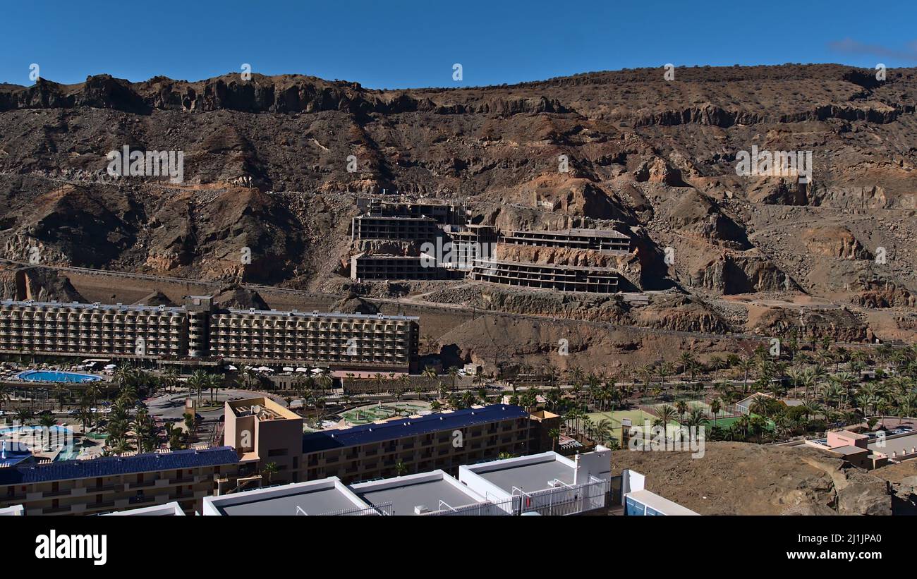 Vue aérienne sur le petit village de Taurito situé dans une vallée dans le sud de Gran Canaria, Espagne avec un bâtiment d'hôtel inachevé sur la pente le jour ensoleillé. Banque D'Images