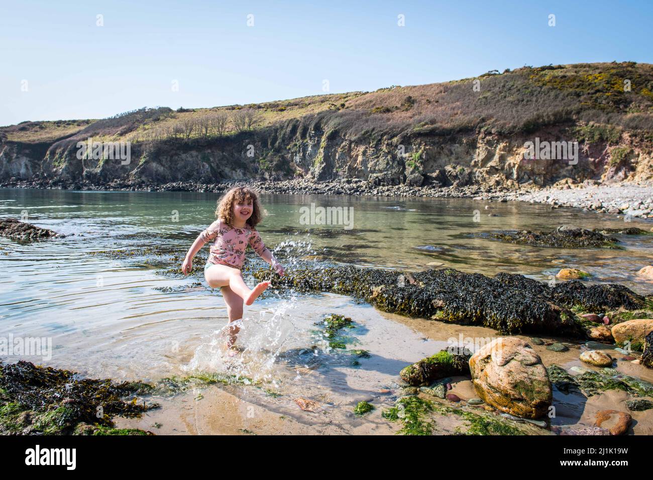 Lillian Joy, âgée de quatre ans, éclabousse dans la mer à la baie de Porthlysgi, près de St Davids dans le Pembrokeshire, le jour le plus chaud de l'année tandis que les gens apprécient le beau temps du printemps dans tout le Royaume-Uni. Banque D'Images