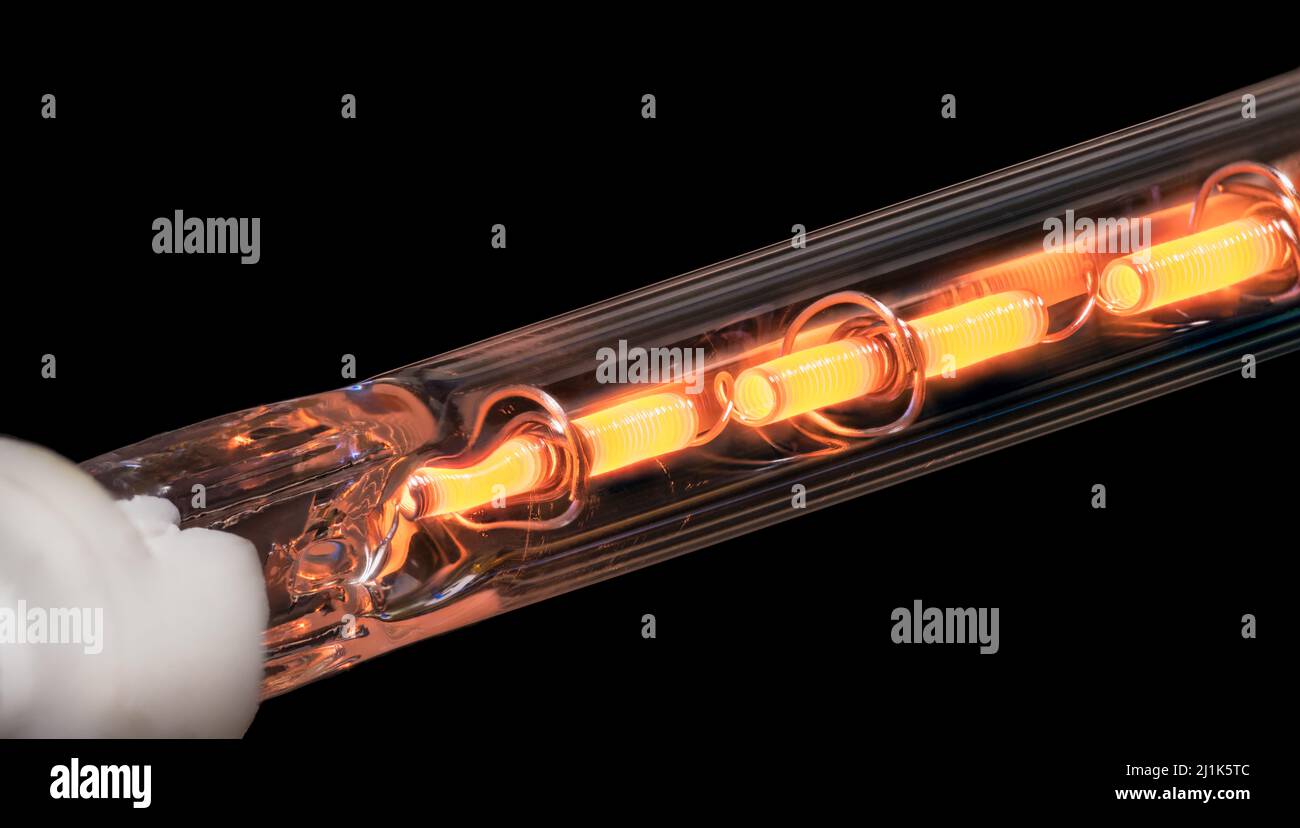Fil de résistance enroulé à l'intérieur de l'élément chauffant sur fond noir. Gros plan du conducteur métallique chaud orange dans le tube en verre du module de finition de l'imprimante laser. Banque D'Images