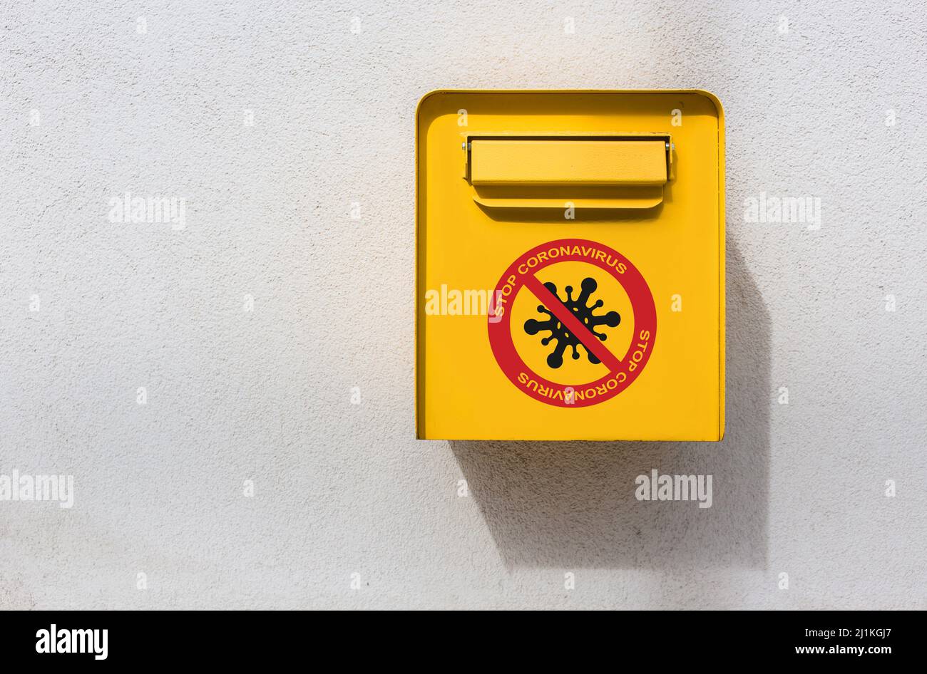 Boîte postale jaune sur le mur avec signe de virus de corona d'arrêt Banque D'Images