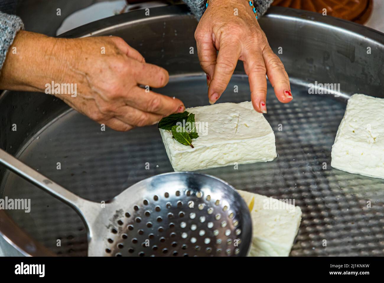 Dans le village d'Akdeniz, qui traduit signifie mer Méditerranée, vous obtenez une impression de la vie typique de pays chypriote. Chaque jour, la fromagère Fatma Haloumi (Hellim), la spécialité chypriote la plus célèbre à base de lait de chèvre et de lait de brebis. Les morceaux Hellim cuits et salés sont frottés à la menthe fraîche. Préparation de la spécialité au fromage Hellim ou Halloumi à Akdemiz, Chypre du Nord Banque D'Images