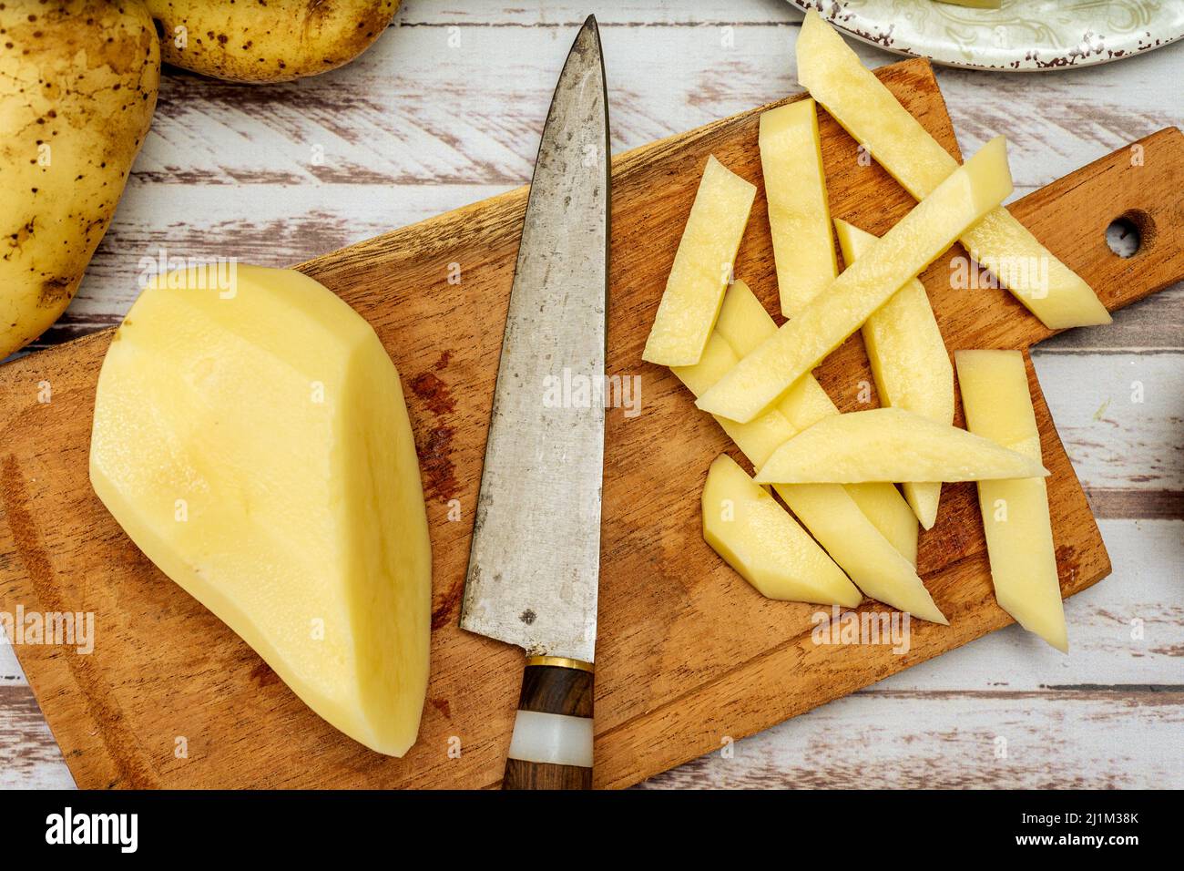 Planche à découper en bois avec pomme de terre coupée en bâton pour faire des frites. Une demi-pomme de terre pelée et un couteau sur une table rustique. Vue de dessus. Banque D'Images