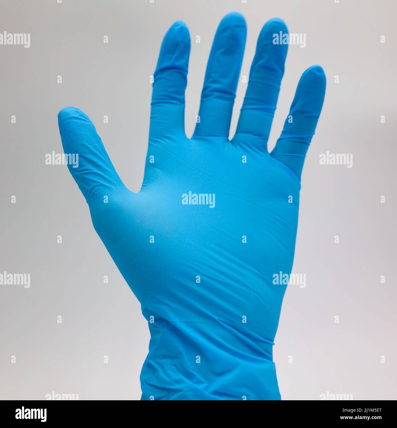 Gants médicaux, de couleur bleue, ne montrant qu'une seule main devant un fond blanc. Banque D'Images