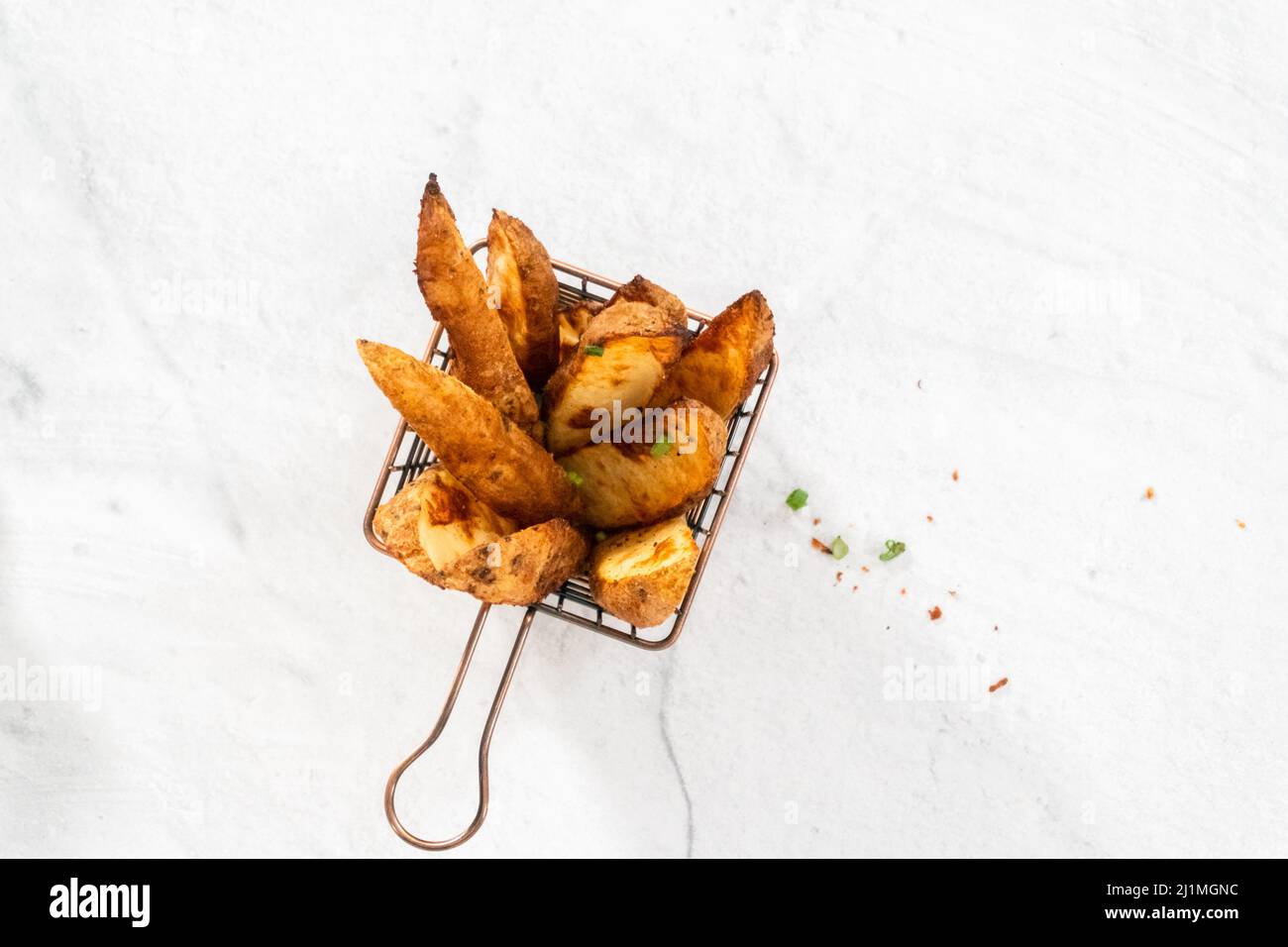 Pose à plat. Quartiers de pommes de terre fraîchement cuits avec épices dans un panier en fil métallique. Banque D'Images