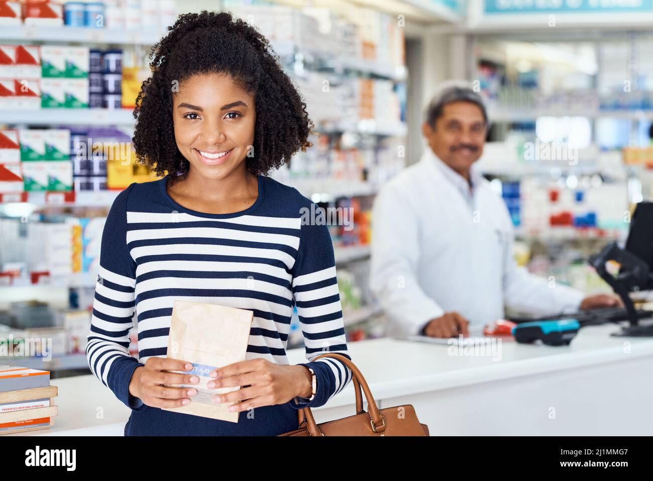 Ma pharmacie locale stocke tout ce dont j'ai besoin. Portrait d'une jeune femme debout dans un chimiste avec un pharmacien en arrière-plan. Banque D'Images