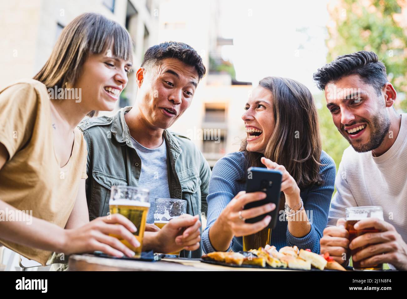 les jeunes s'amusent à la brasserie, une femme rieuse plaisantant avec des amis, regardant un smartphone, un jeune homme asiatique faisant un visage amusant - lixivials lif Banque D'Images