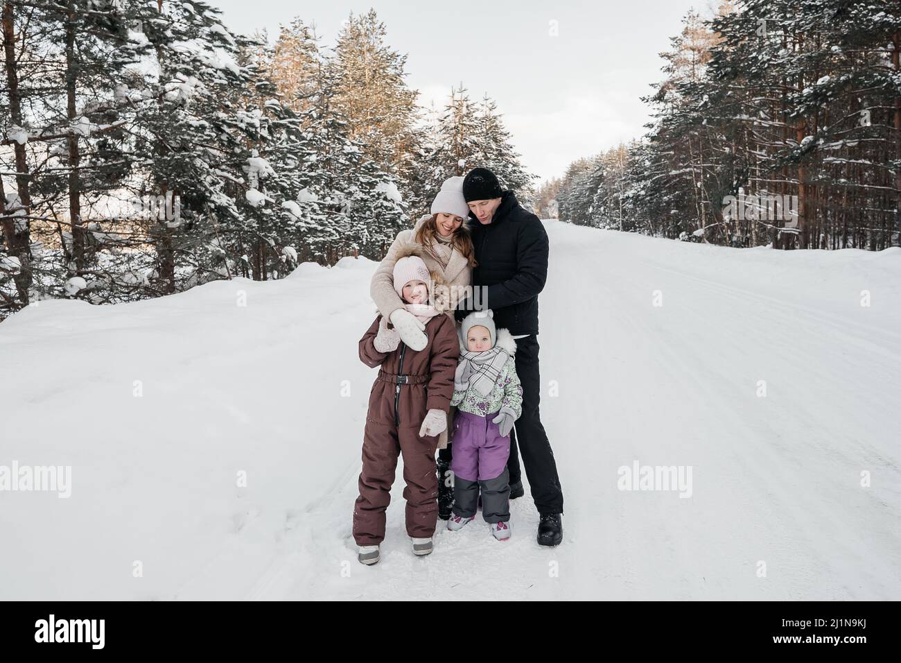 papa, maman et deux filles marchent à travers la forêt enneigée Banque D'Images