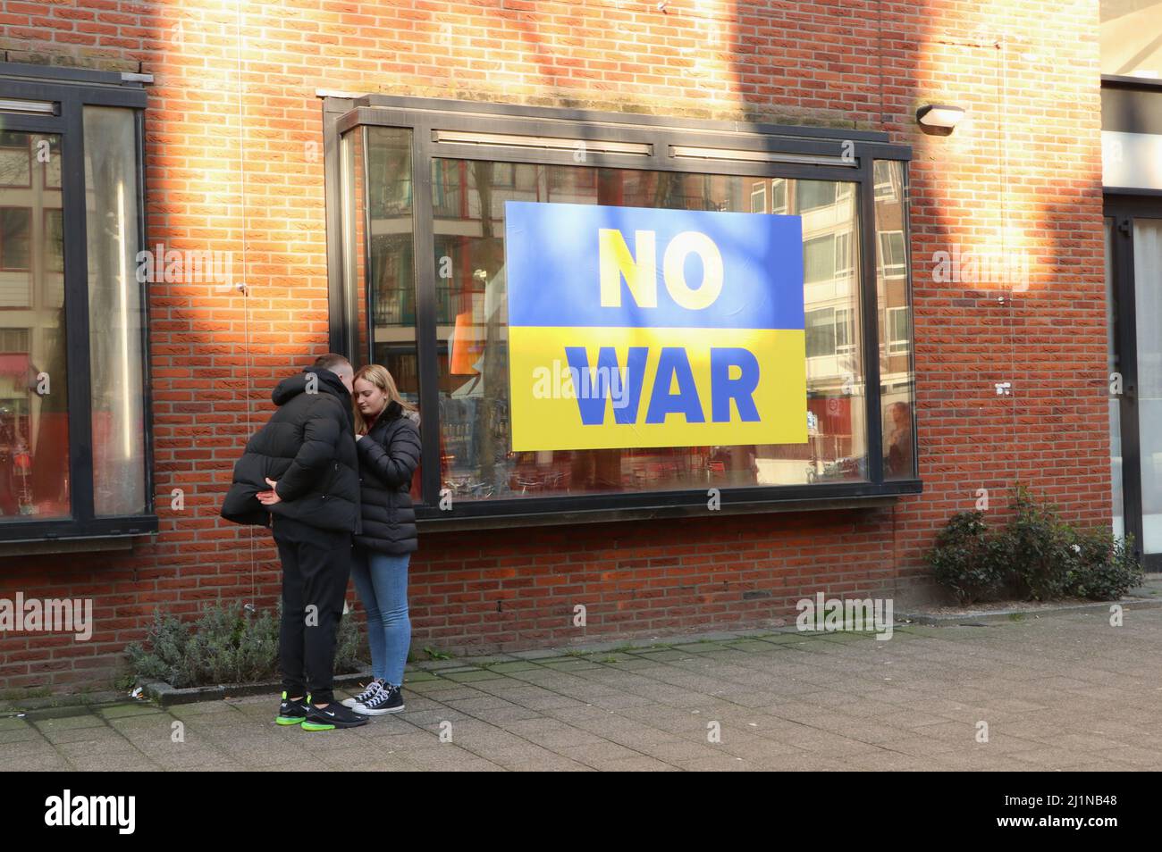 Jeune couple debout à côté d'aucune bannière de guerre contre la guerre en Ukraine dans la vitrine de magasin dans le centre-ville d'Amsterdam, pays-Bas Banque D'Images