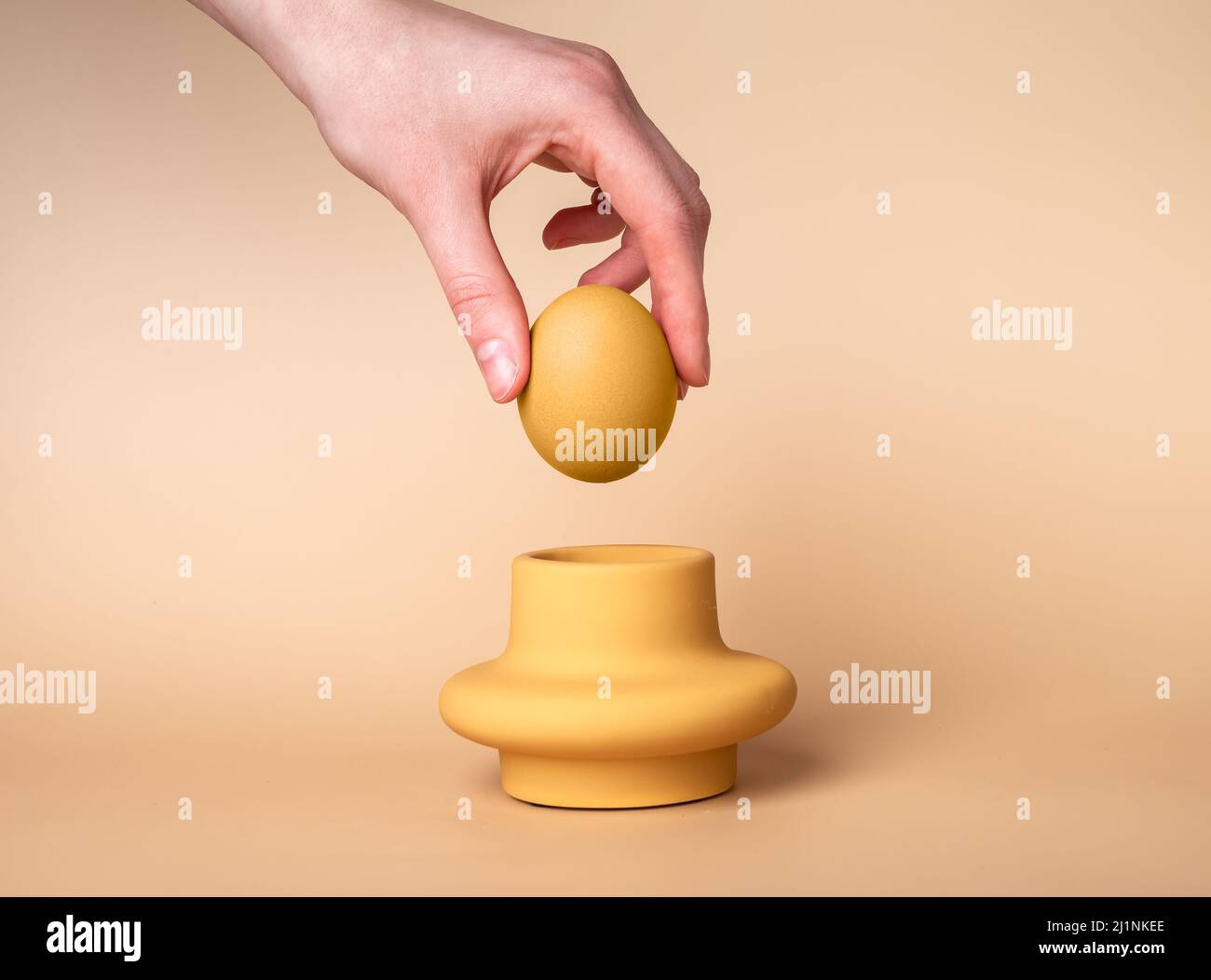 Femme à la main mettant l'œuf beige dans la tasse. Porte-œufs et serveur. Concept de Pâques. Photo de haute qualité Banque D'Images