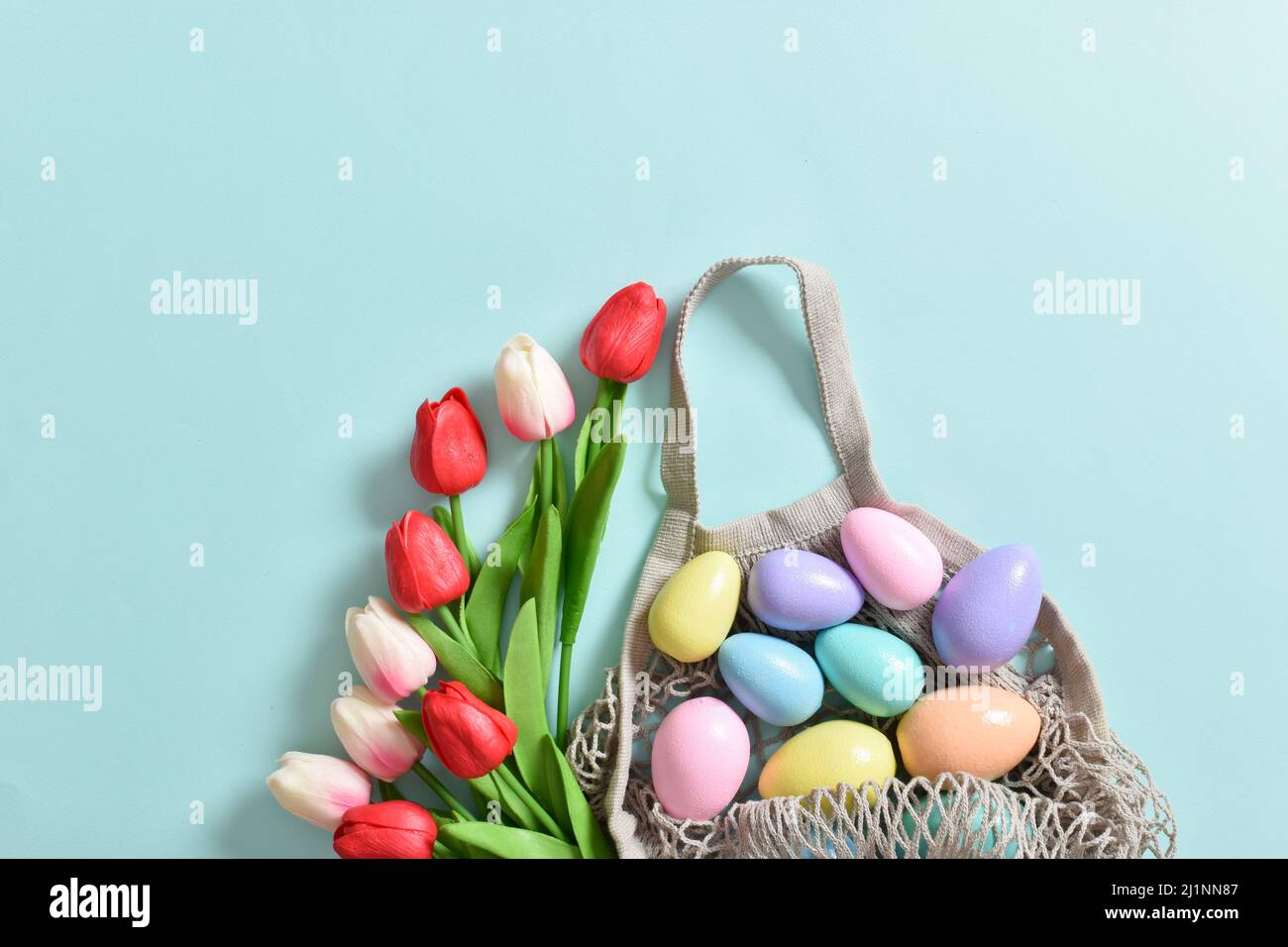 Un beau bouquet de tulipes avec un sac à cordes contenant des œufs peints. Bannière pour les joyeuses fêtes de Pâques Banque D'Images