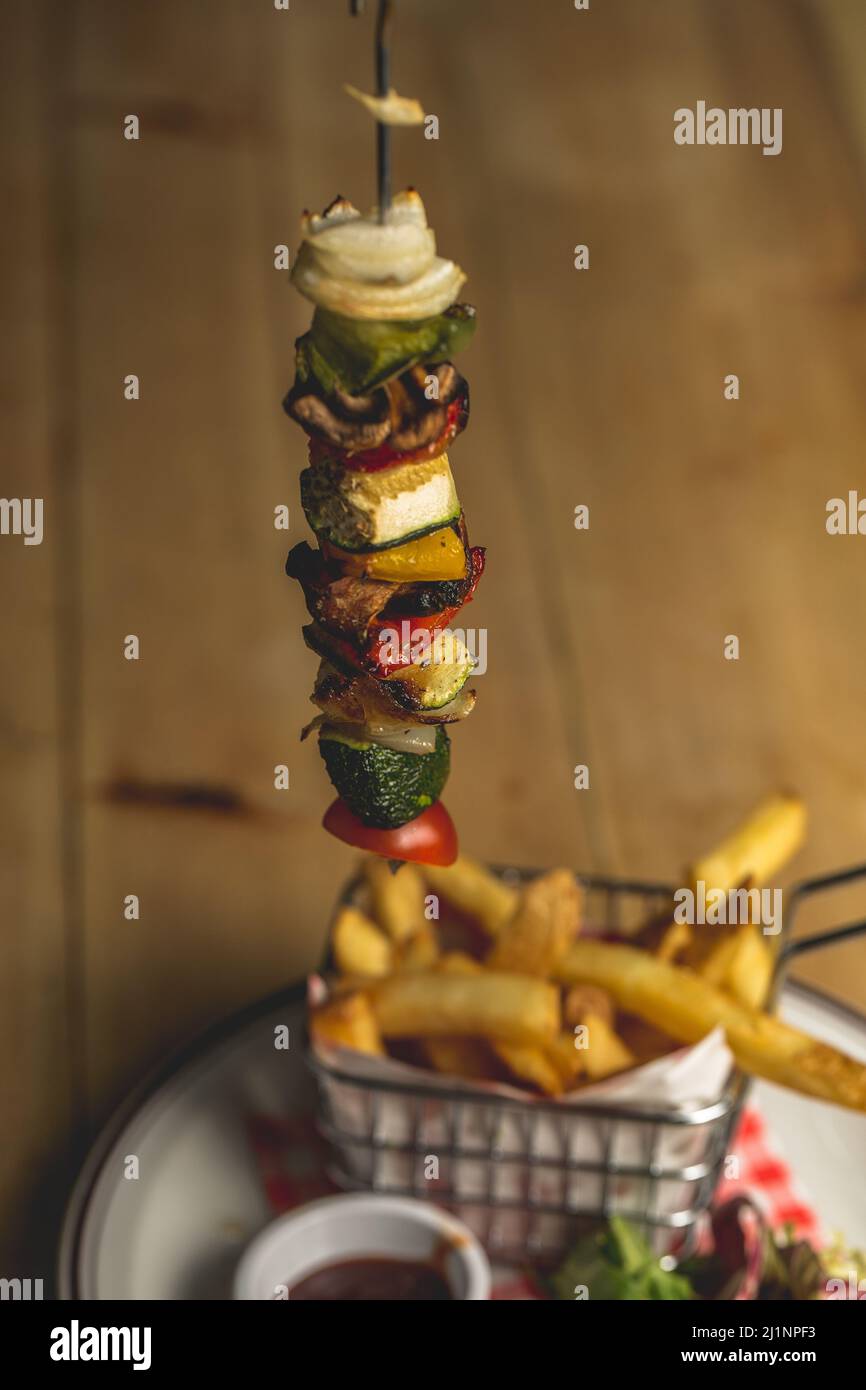 Un gros plan d'un kebab suspendu (viande grillée avec légumes) servi avec des frites Banque D'Images