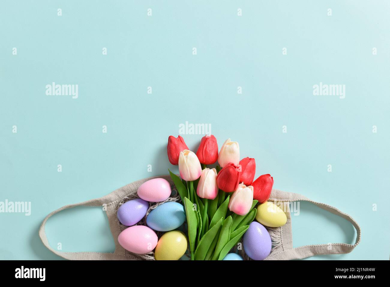 Un beau bouquet de tulipes avec un sac à cordes contenant des œufs peints. Banque D'Images