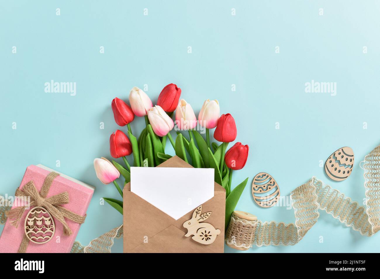 Un beau bouquet de tulipes avec une carte postale et un cadeau et des oeufs de Pâques en bois sur fond bleu clair. Banque D'Images