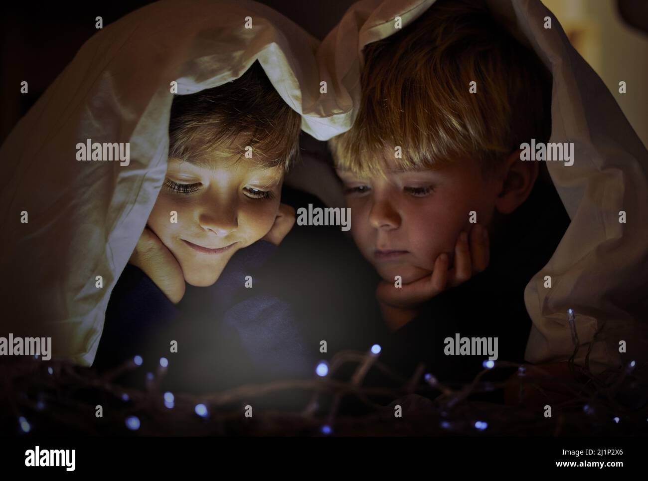 Voyez la vie avec des yeux enfantin, ils ne manquent jamais les fées. Photo de deux adorables petits garçons à l'aide d'une tablette numérique sous une couverture de fort la nuit à l'intérieur Banque D'Images