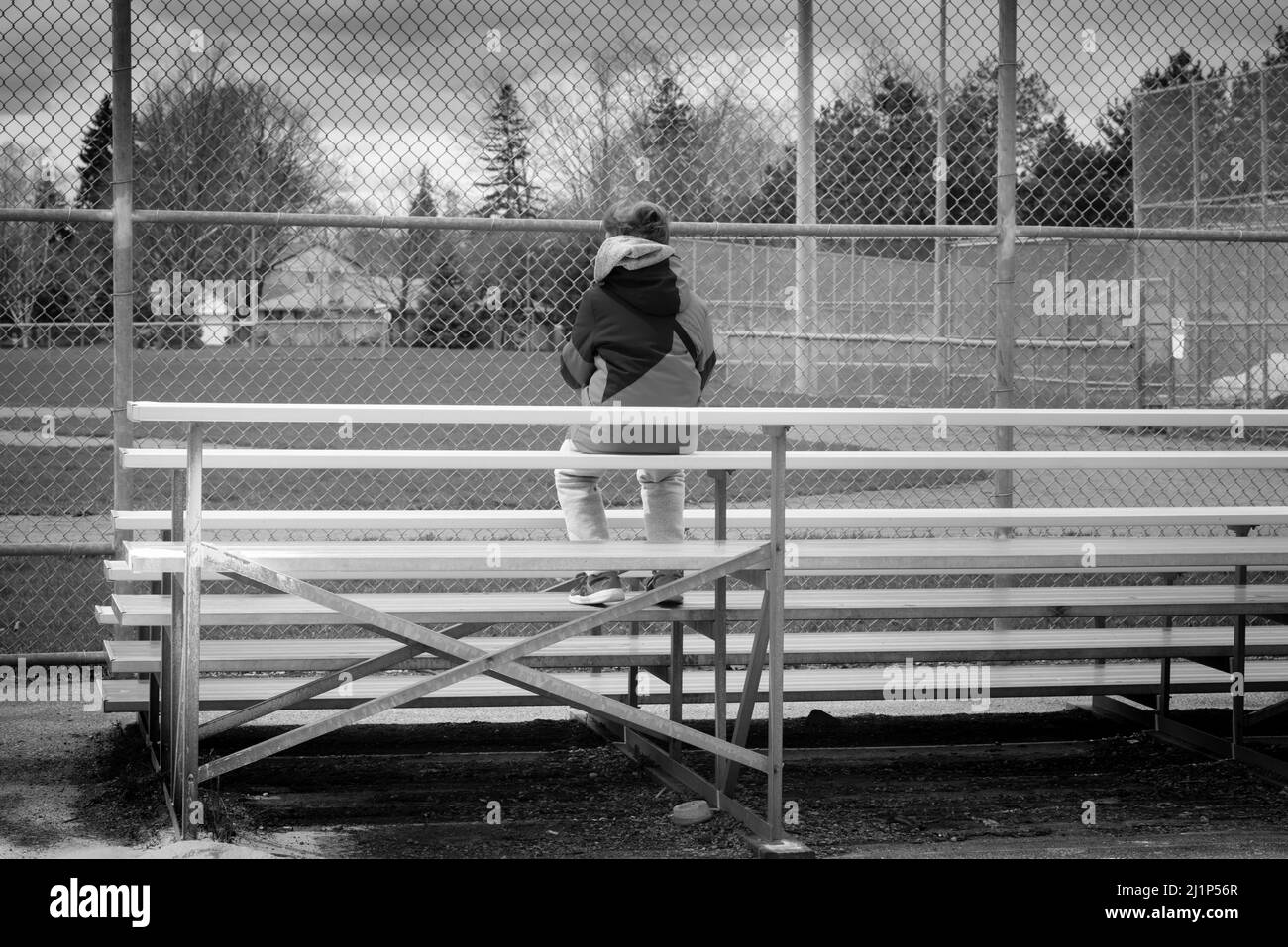 Un jeune garçon assis dans les gradins au diamant de baseball. En attente du début du baseball de la pandémie COVID-19. Banque D'Images