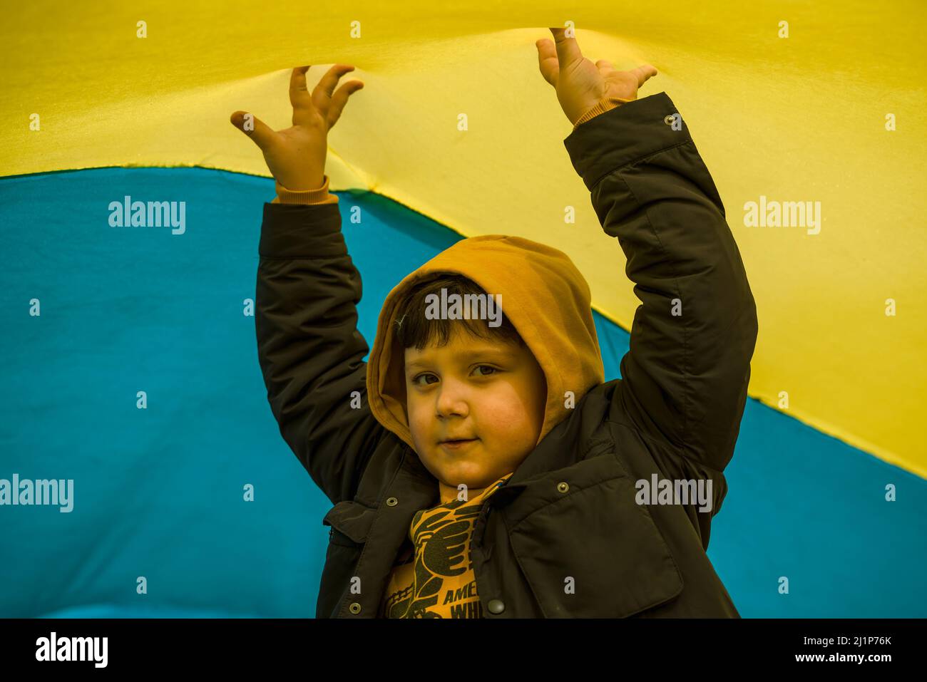 Barcelone, Espagne. 27th mars 2022. Un garçon ukrainien joue sous un drapeau géant lors d'une manifestation pour exiger des actions pour arrêter les attaques russes après plus d'un mois de guerre. Credit: Matthias Oesterle/Alamy Live News Banque D'Images