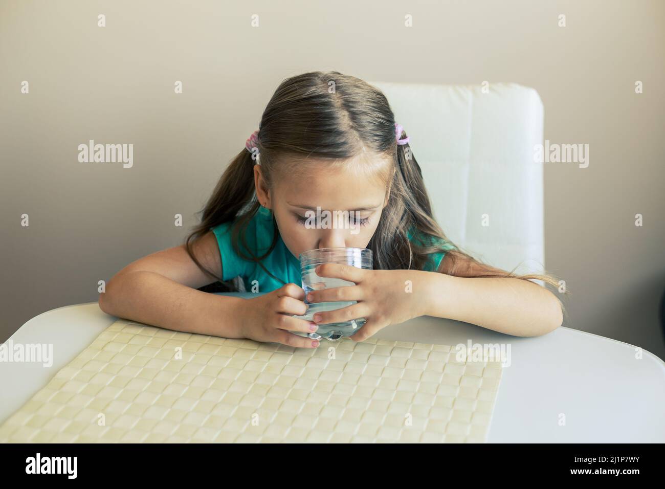 Belle petite fille boit de l'eau propre d'un verre transparent. Banque D'Images