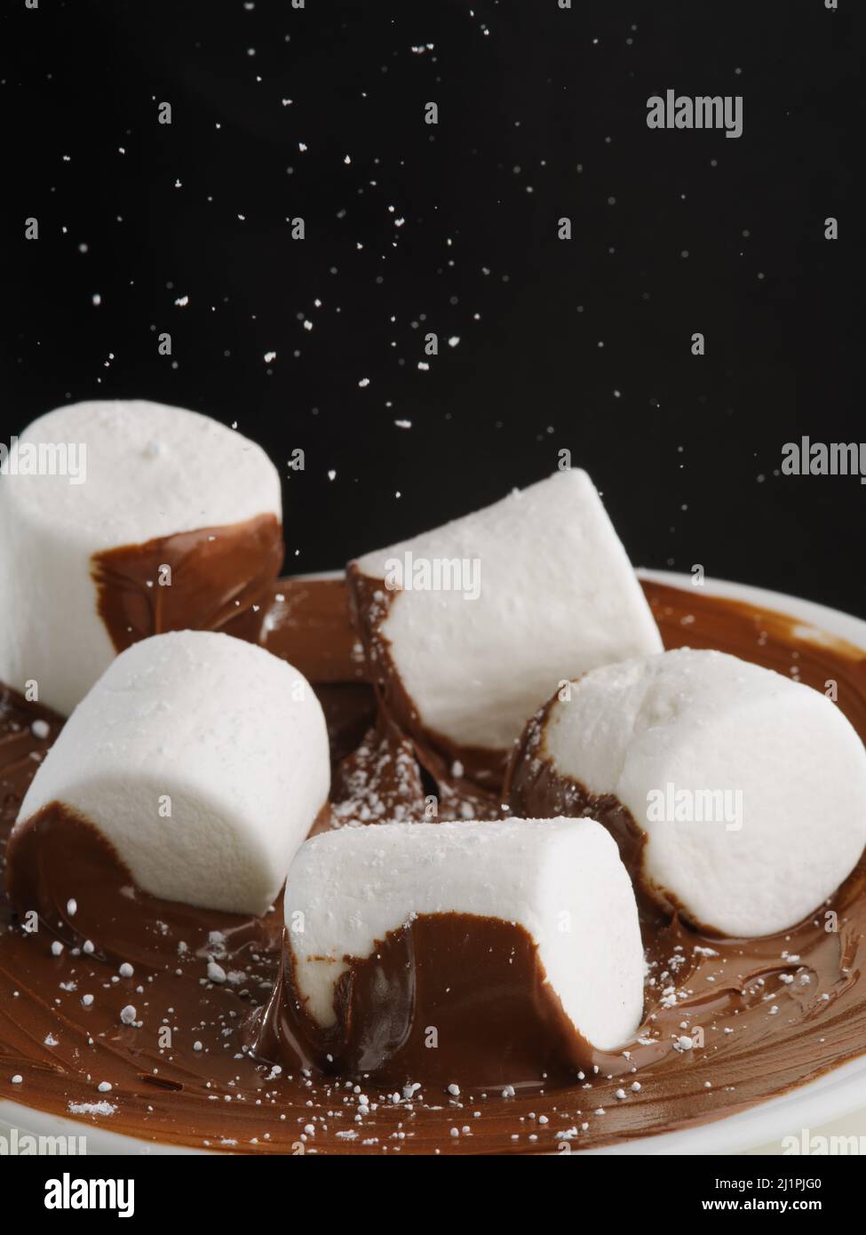 Morceaux de guimauve en pâte de chocolat. Sur fond noir, la chapelure de sucre blanche dans un vol gelé. Délicieux bonbons, petit déjeuner américain, pâtisserie, Banque D'Images