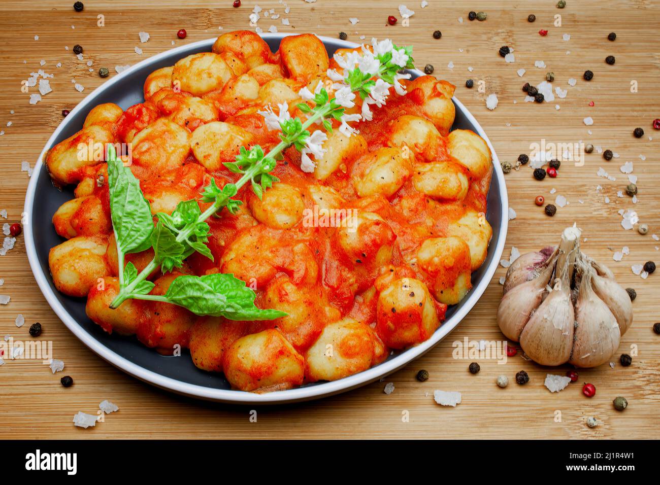 Gnocchi italien maison traditionnel dans une sauce tomate aromatique servi sur une assiette décorative et garni d'herbes, de basilic, de poivre coloré, d'ail et Banque D'Images