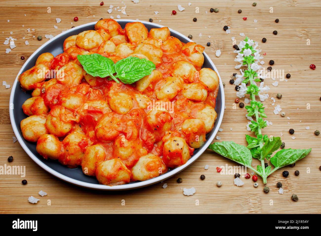 Gnocchi italien maison traditionnel dans une sauce tomate aromatique servi sur une assiette décorative et garni d'herbes, de basilic, de poivre coloré, d'ail et Banque D'Images