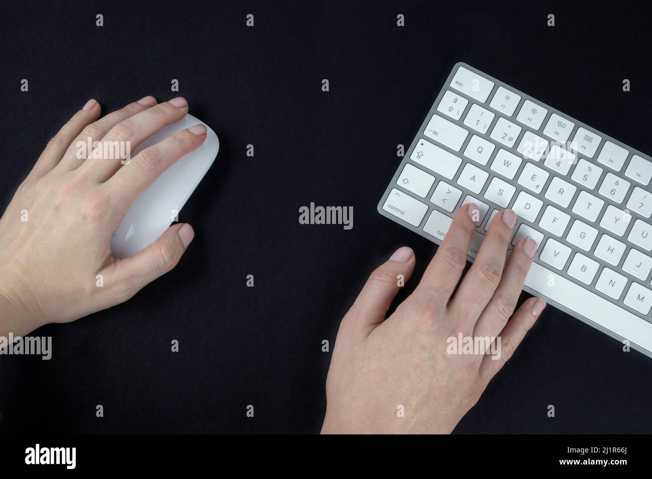 Une femme gaucher tient une souris d'ordinateur dans sa main gauche. Clavier  blanc et argent sur fond noir Photo Stock - Alamy