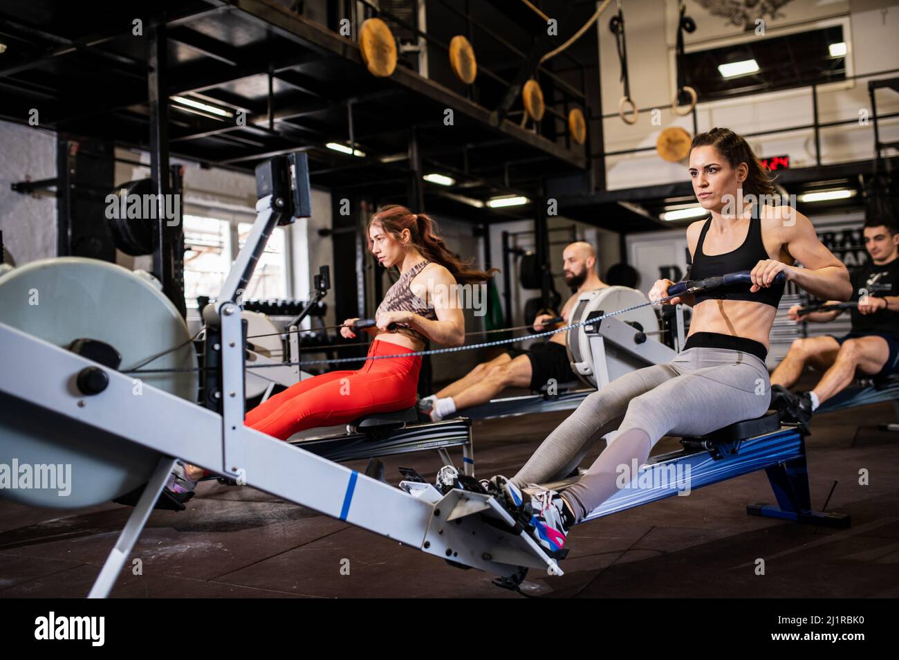 Formation de groupe. Quatre jeunes dans une salle de gym entièrement équipée et moderne font de l'exercice lourd pour tout le corps et transpirent dans leur caillot sportif Banque D'Images