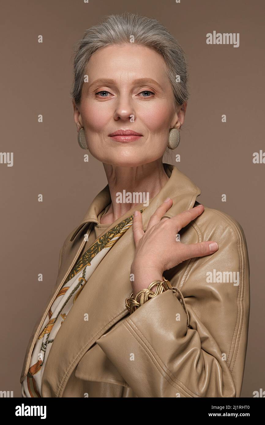 Portrait d'une belle femme âgée en imperméable beige avec maquillage classique et cheveux gris. Banque D'Images