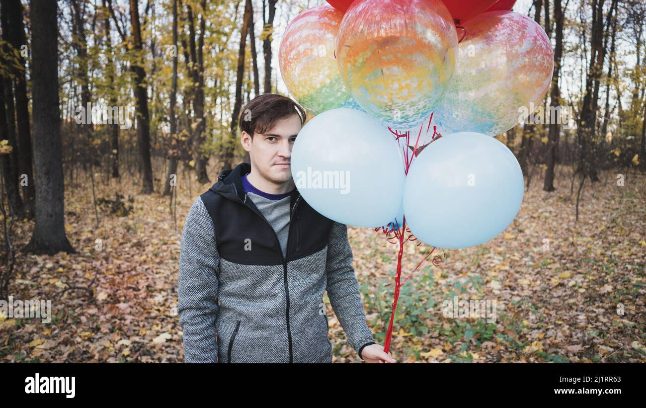 Un jeune homme beau tient les ballons colorés sur la promenade dans la forêt d'automne Banque D'Images