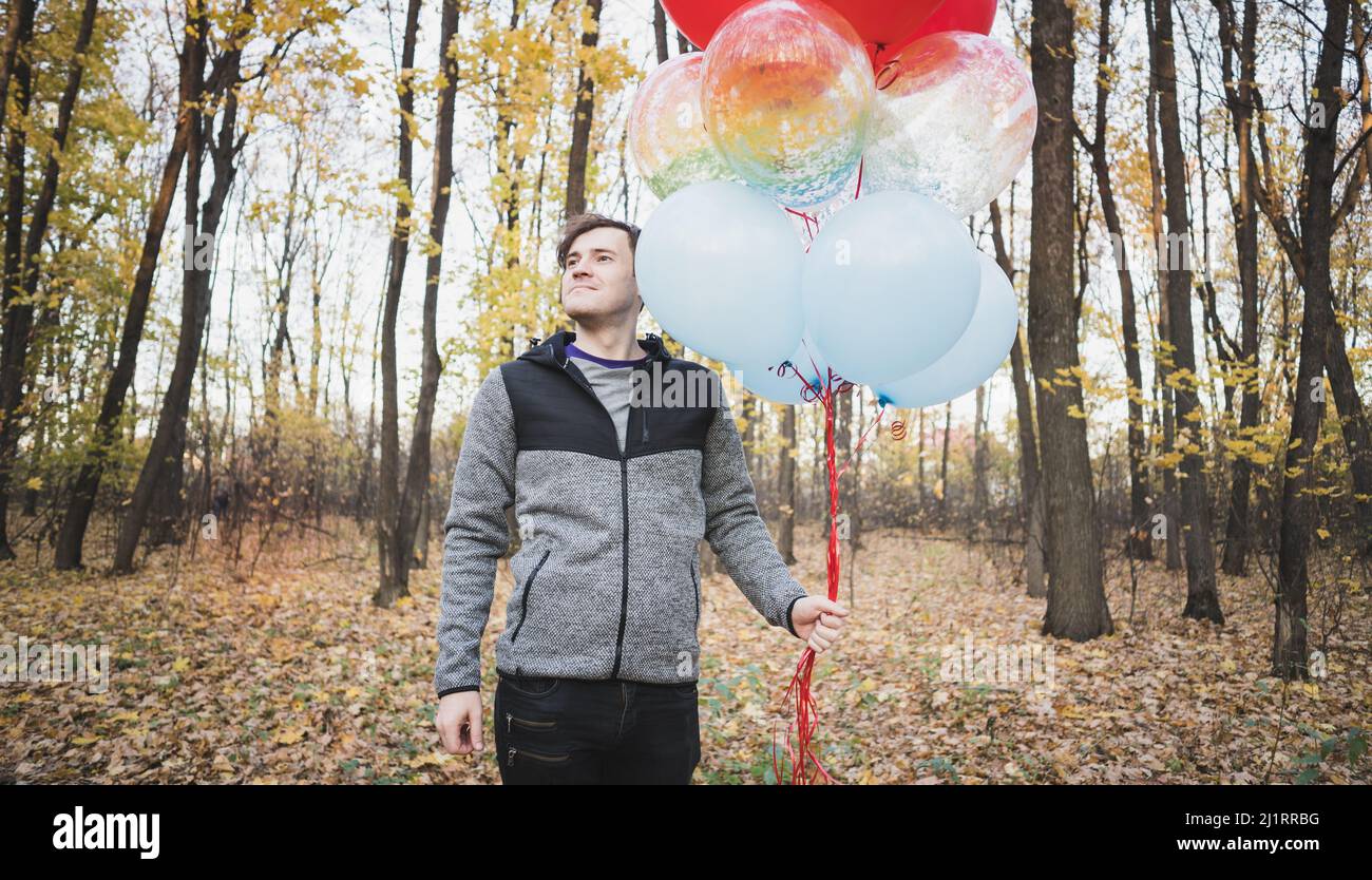 Un jeune homme beau tient les ballons colorés sur la promenade dans la forêt d'automne Banque D'Images