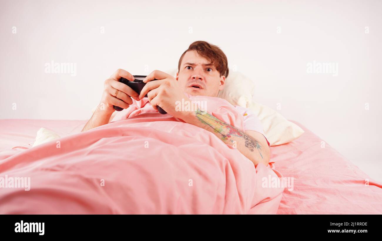 Homme avec joystick jouant à un jeu vidéo allongé sur le lit. Un jeune homme avec un joystick, addiction de jeu Banque D'Images