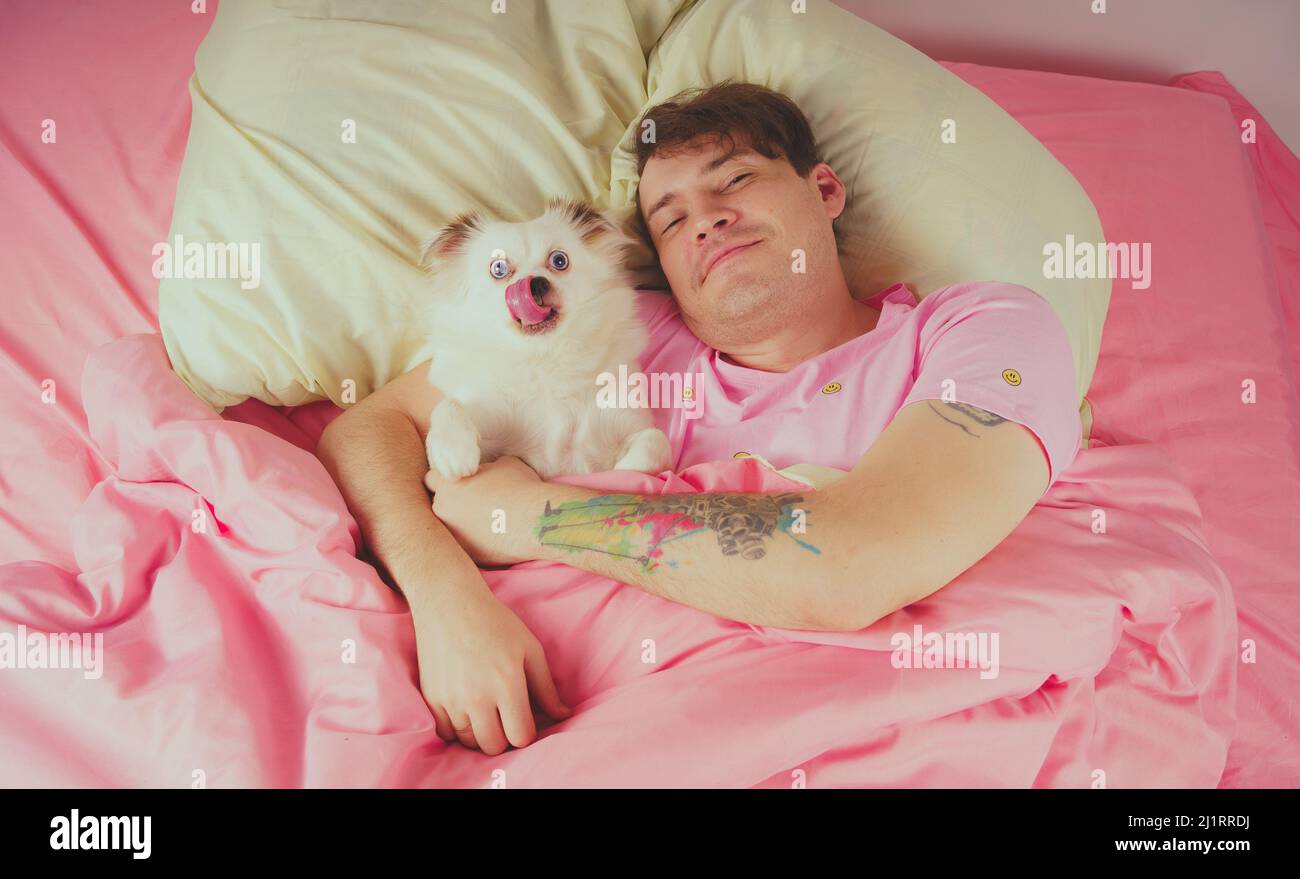 Bel homme allongé avec un chien au lit. Jeune homme dans un lit sous un tapis avec son chien dans une étreinte Banque D'Images