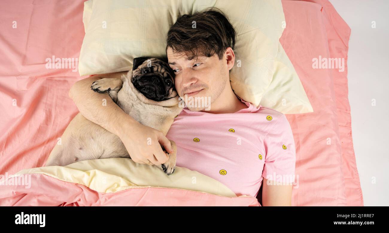 Bel homme allongé avec un chien au lit. Jeune homme dans un lit sous un tapis avec son chien dans une étreinte Banque D'Images