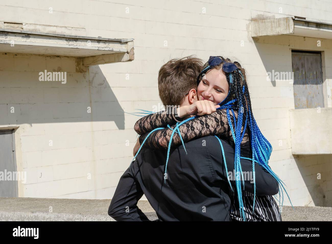 Un jeune couple hétérosexuel est en cuddling à l'extérieur. L'homme dans la chemise noire berce la femme avec les longues dreadlocks bleues. Amoureux ou jeune famille. Banque D'Images