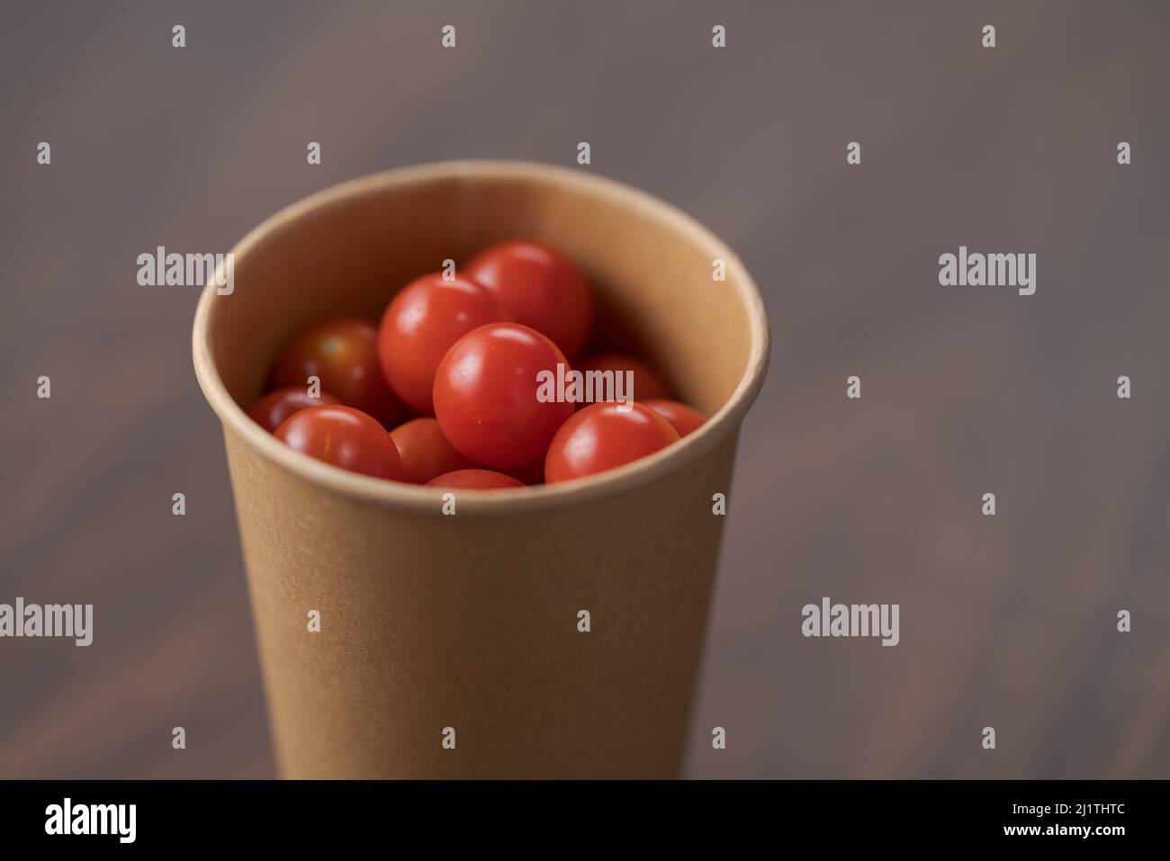 Tomates cerises dans un récipient en papaper sur une table en bois, mise au point peu profonde Banque D'Images