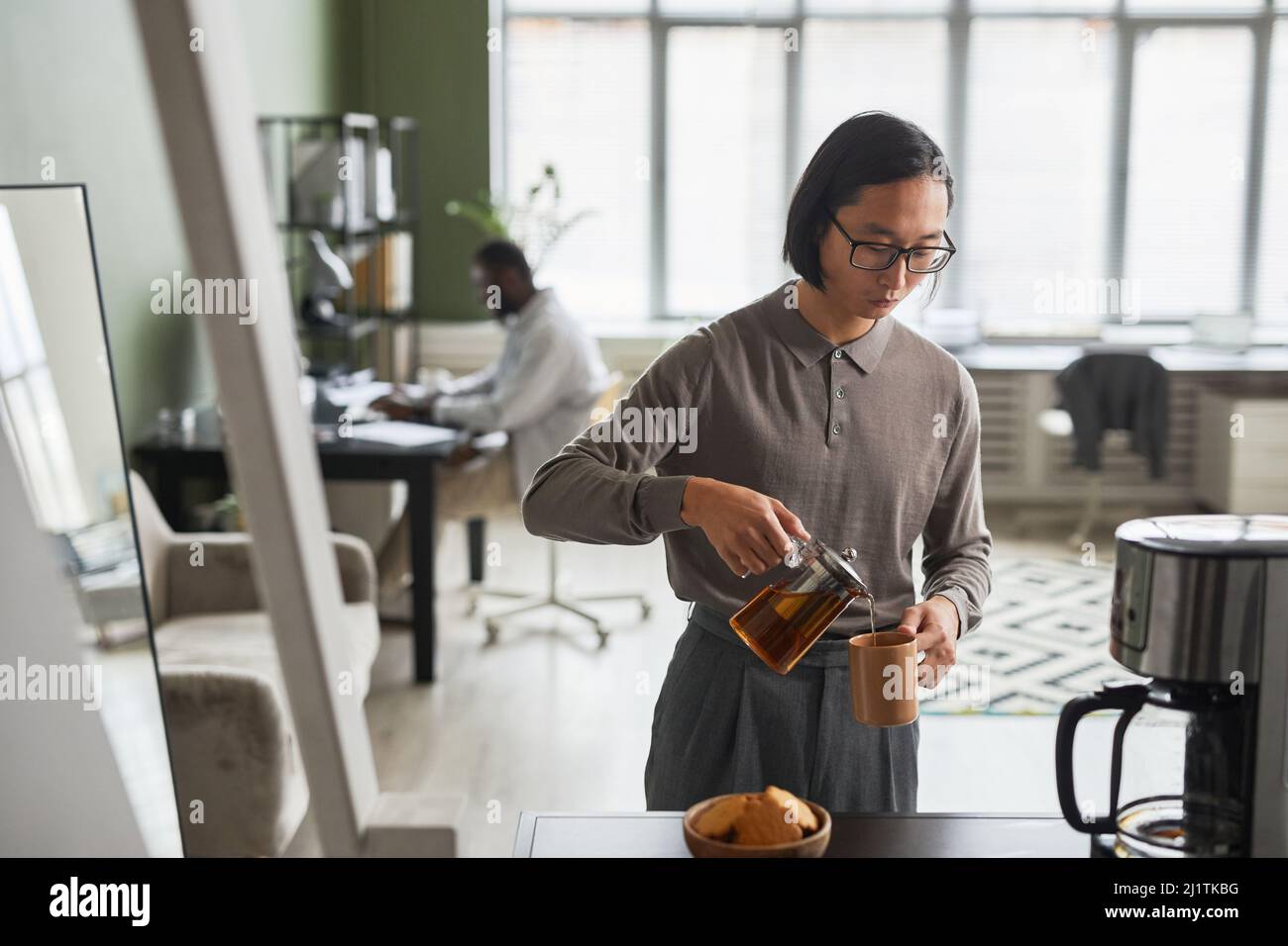 Mini portrait de la taille vers le haut du jeune homme asiatique faisant du café au bureau et portant gris, espace de copie Banque D'Images