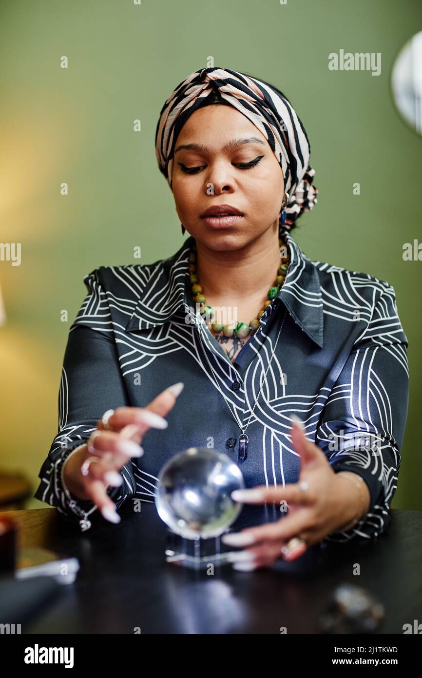 Portrait vertical de la fortune ethnique qui regarde dans la boule de cristal à la seance spirituelle dans le magasin Banque D'Images
