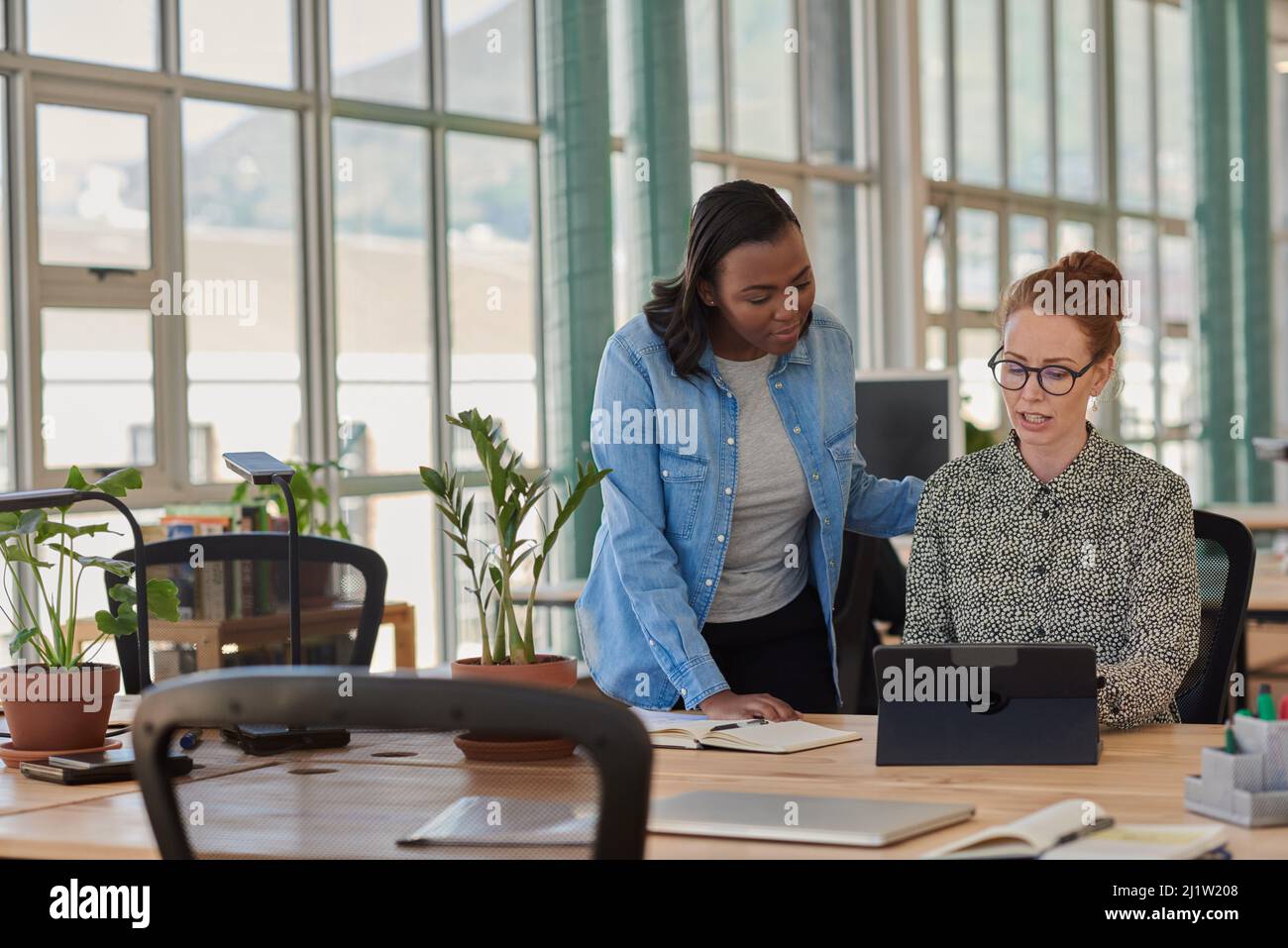 Deux femmes d'affaires diverses travaillant sur une tablette à un bureau Banque D'Images