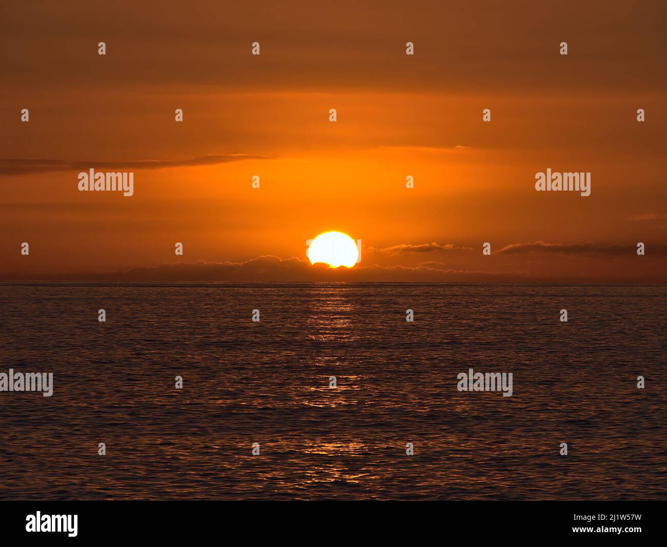 Coucher de soleil au-dessus de l'océan Atlantique avec un soleil éclatant qui disparaît entre les nuages bas à l'horizon et le ciel orange vu de la côte de Gran Canaria. Banque D'Images