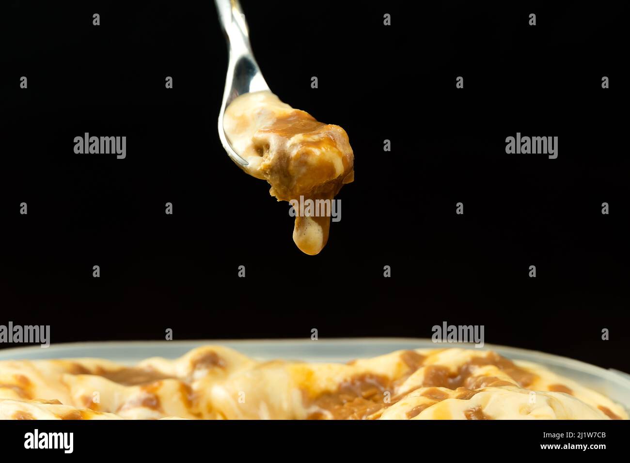 Photo macro d'une cuillère à dessert avec crème glacée au caramel sur un contenant de crème glacée en face d'un fond noir avec espace de copie. Banque D'Images