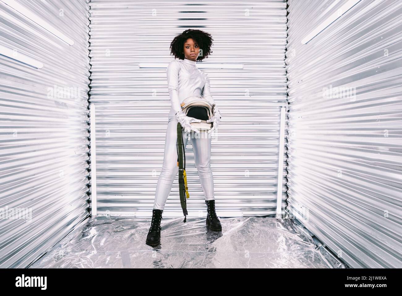Charmante femme afro-américaine avec casque en costume d'astronaute blanc regardant la caméra tout en se tenant dans un vaisseau spatial blanc sur fond clair Banque D'Images